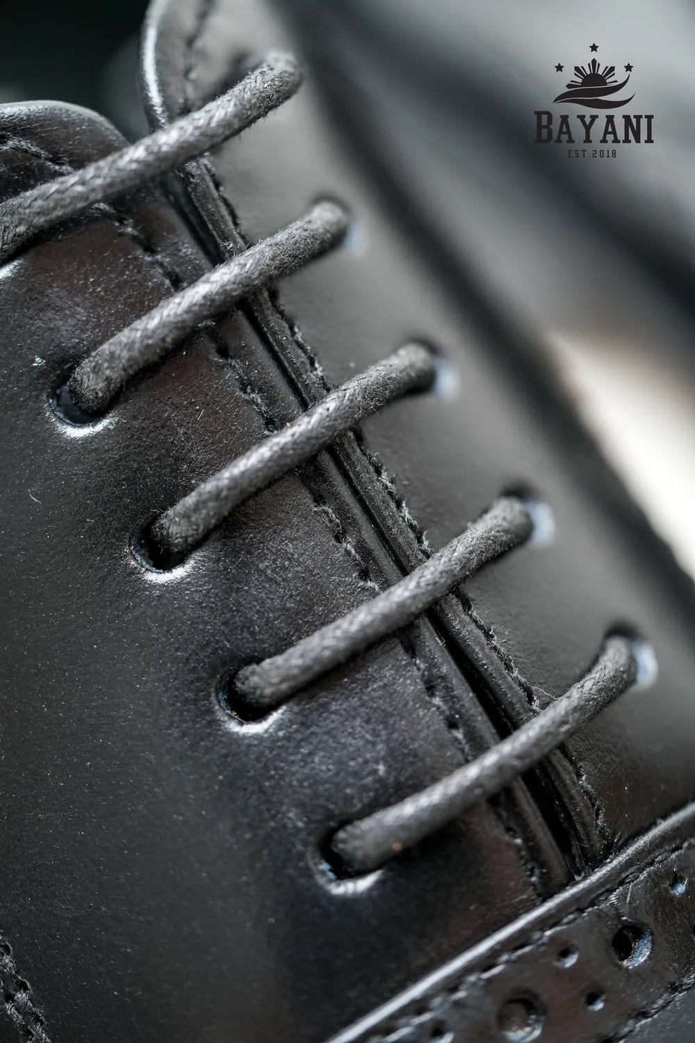Close-up of a black leather shoe with laces, featuring the Bayani logo.
#color_black