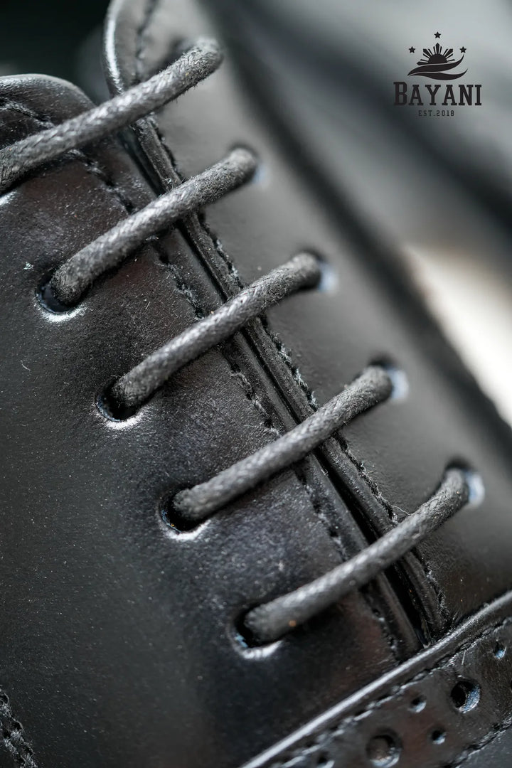 Close-up of a black leather shoe with laces, featuring the Bayani logo.
