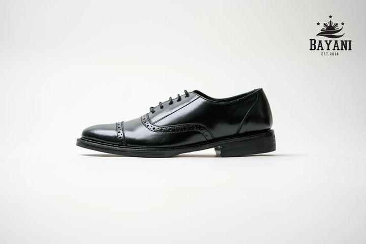 Black dress shoe on a light gray background with Bayani logo.

