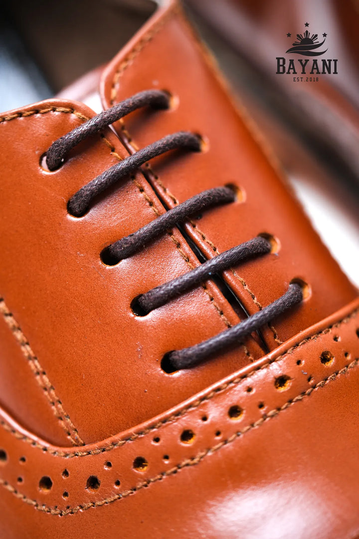 Close-up of a brown leather shoe with black laces, featuring the Bayani brand logo.
