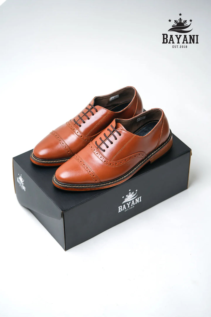 Brown leather shoes on a black box with Bayani logo, on a white background
