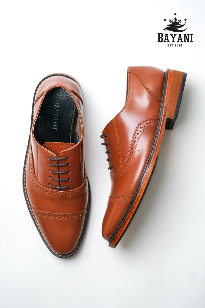 Pair of brown dress shoes on a white background with Bayani logo.
