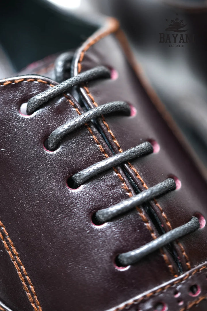 Close-up of a brown leather shoe with black laces, featuring the BAYANI brand.
