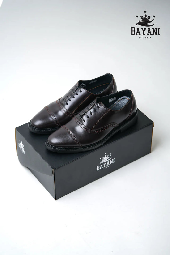 Pair of black dress shoes on a Bayani branded box with the Bayani logo above.
