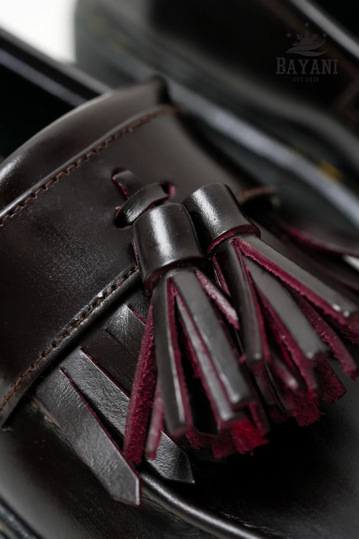 Close-up of a brown leather shoe with a tassel, featuring the brand &