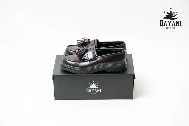 Black loafers with tassels on a black box, featuring the Bayani logo.
