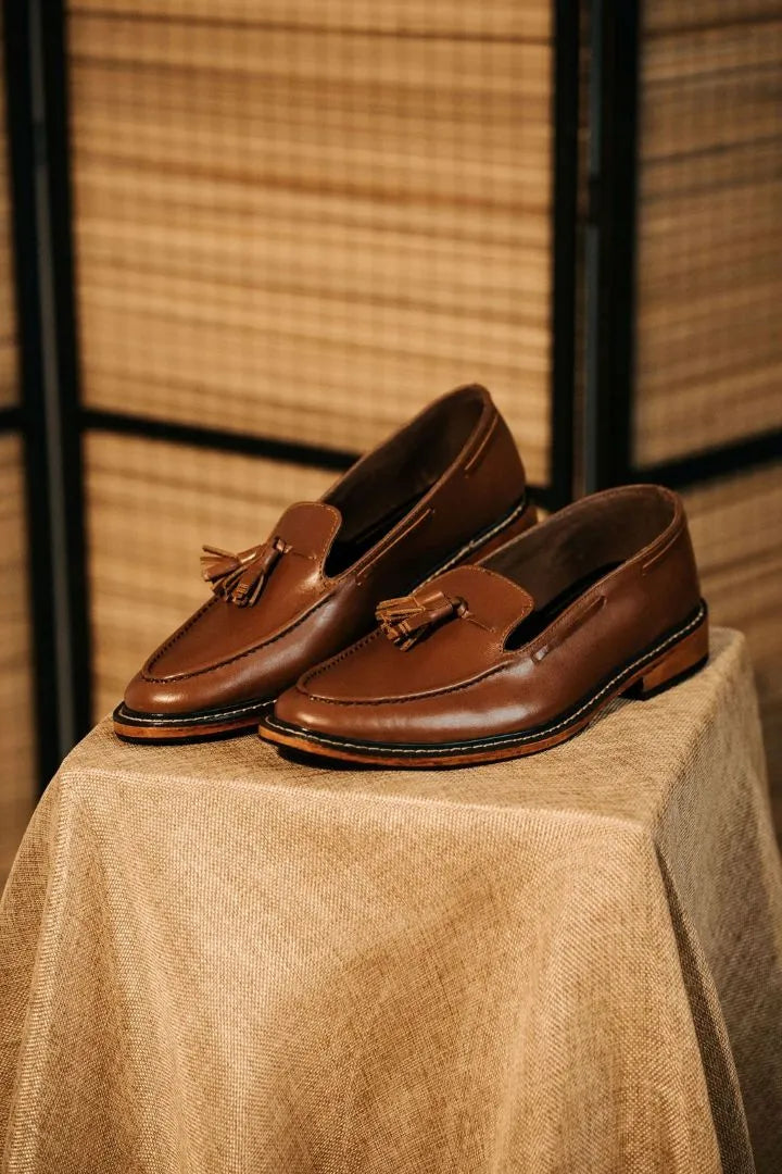 Pair of brown loafers with tassels on a textured surface