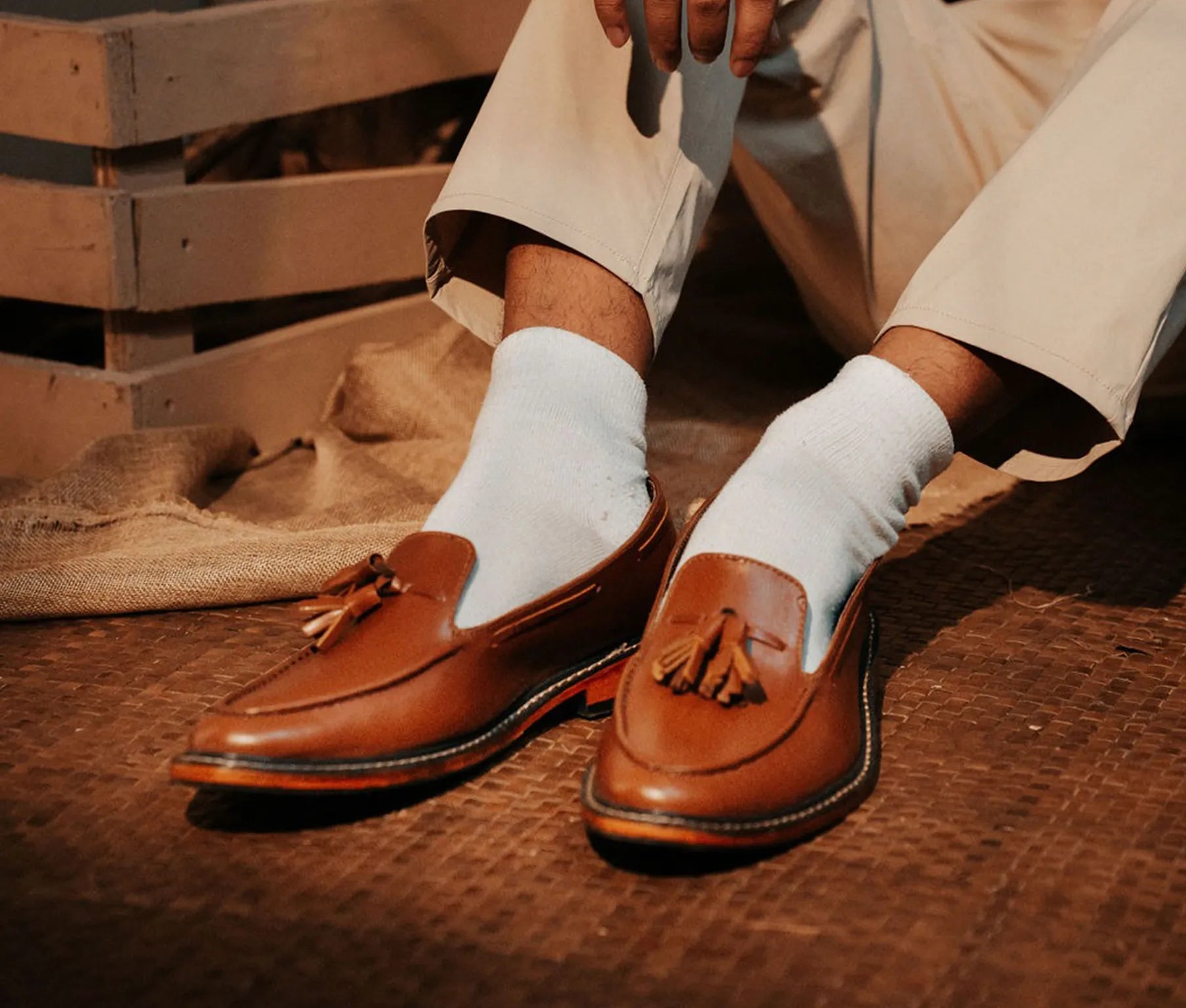Brown loafers with tassels worn with white socks on a wooden floor.