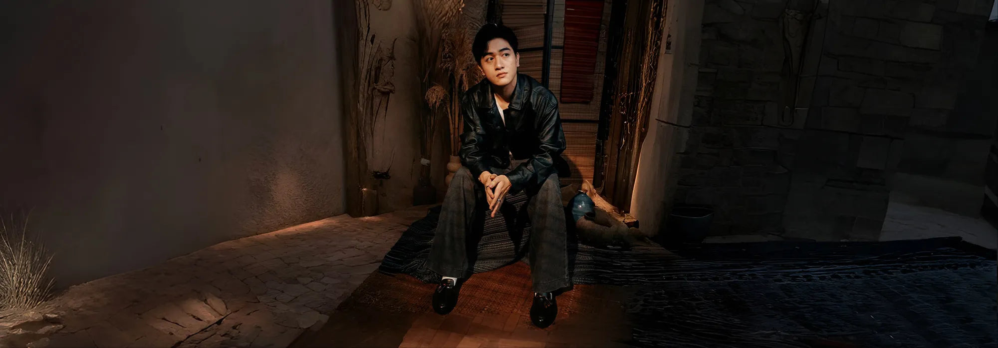 A man wearing a dress shoes sitting on a stone floor in a dimly lit room with wooden beams.