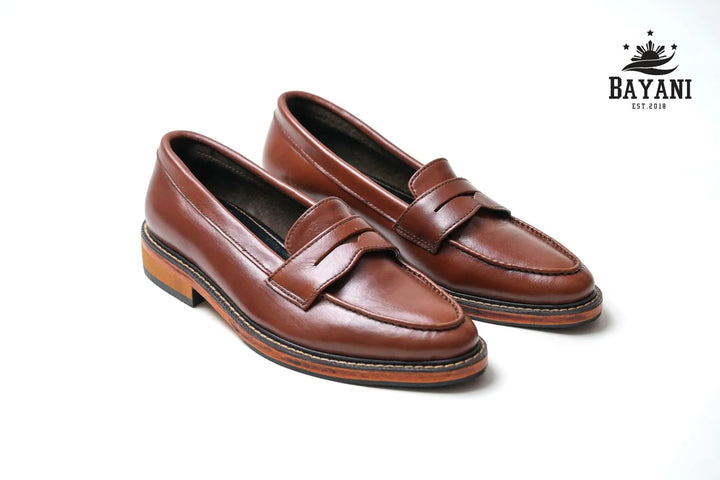 Pair of brown loafers on a white background with Bayani logo.
