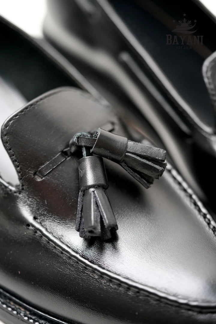 Black leather loafer with tassel detail on a blurred background
