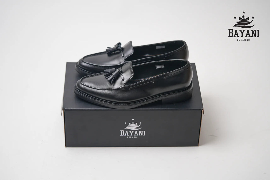 Black loafers with tassels on a black box, featuring the Bayani brand logo.
