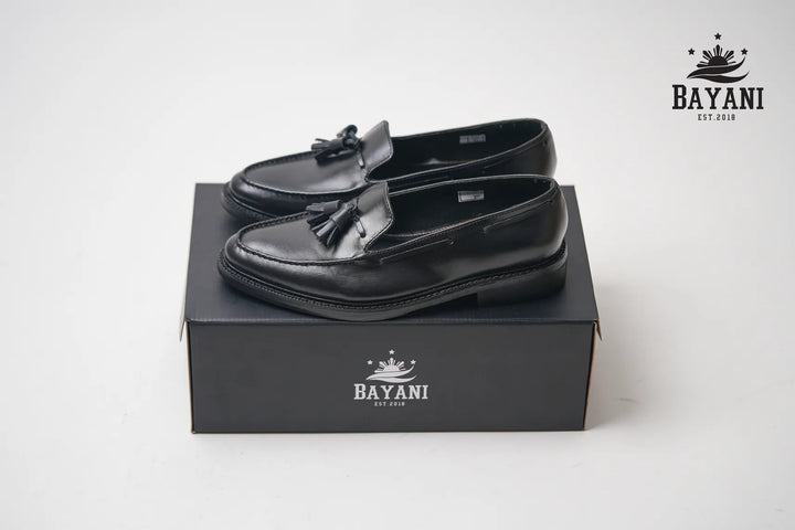 Black loafers with tassels on a black box, featuring the Bayani brand logo.
