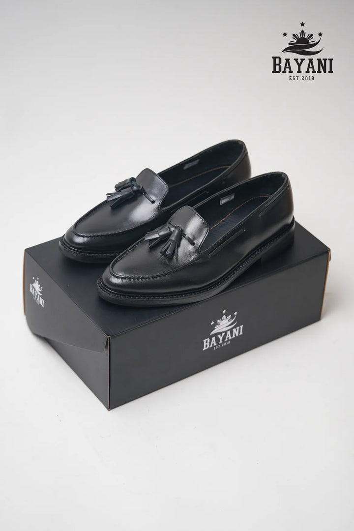 Black loafers with tassels on a black box, featuring the Bayani logo.
