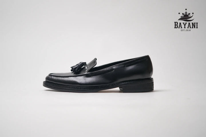 Black loafer shoe with a tassel on a light gray background, featuring the Bayani brand logo.
