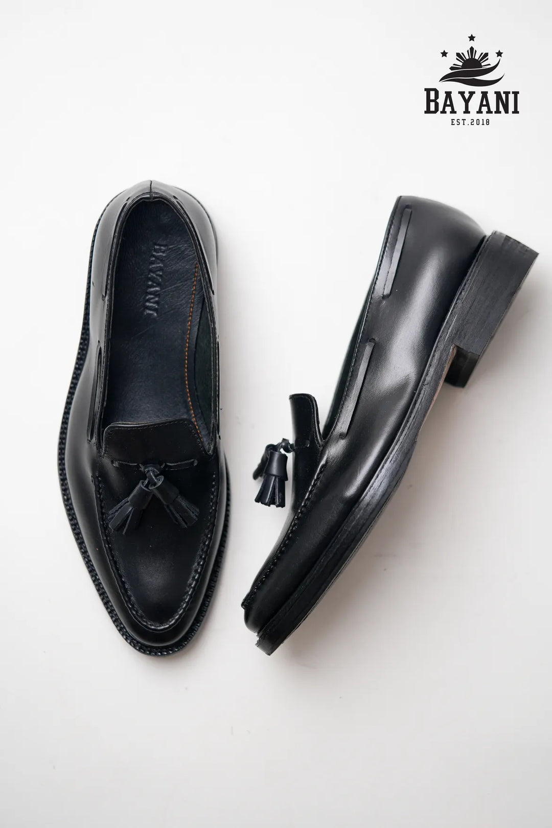 Black loafers with tassels on a white background, featuring the Bayani brand.
