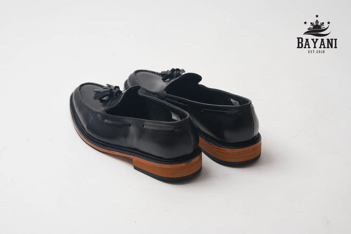 Black loafers with brown soles on a white background, featuring the Bayani logo.
