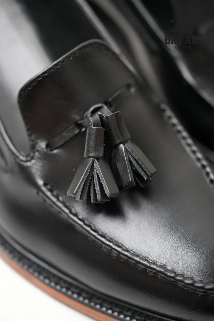 Close-up of a black leather loafer with tassels on a white background
