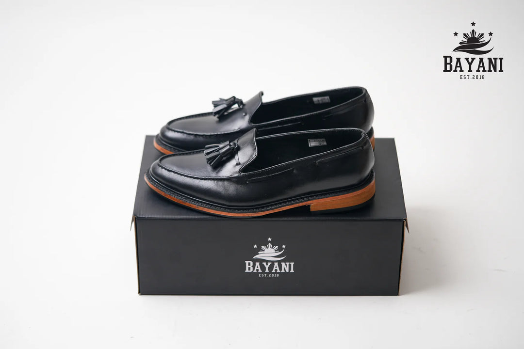 Black loafers with tassels on a black box, featuring the Bayani logo.
