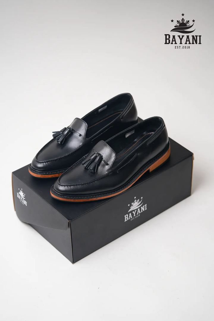 Black loafers with tassels on a black box, featuring the Bayani brand logo.
