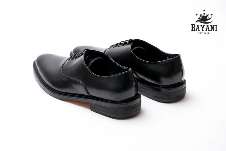 Pair of black dress shoes on a white background with Bayani logo.
