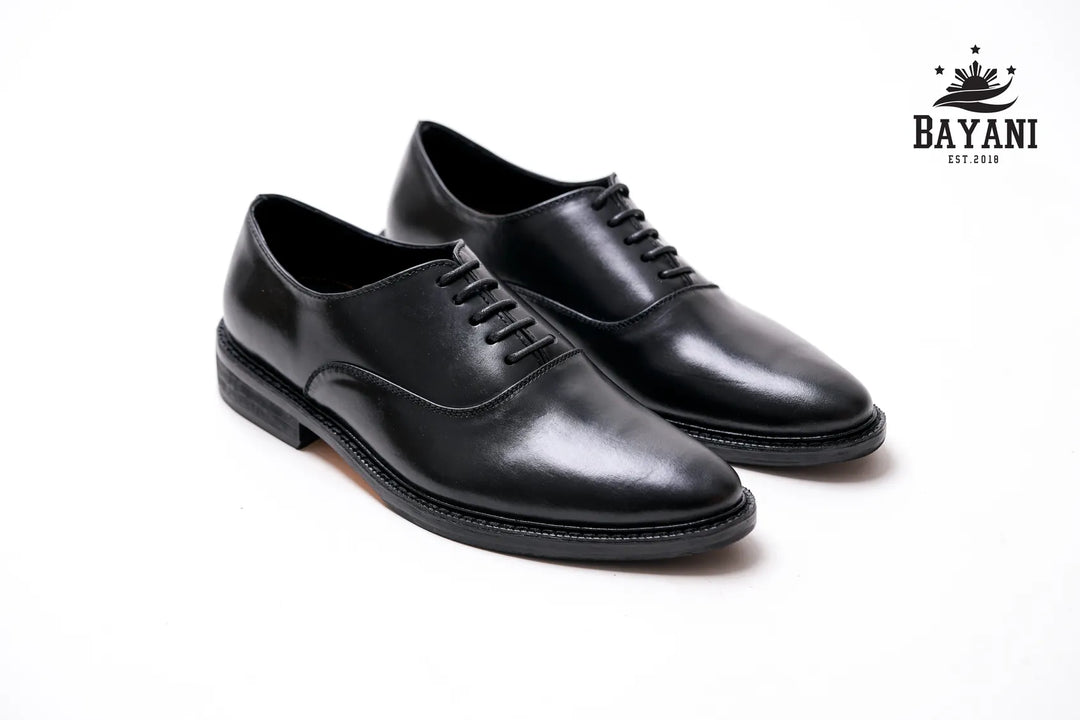 Pair of black dress shoes on a white background with Bayani logo.
