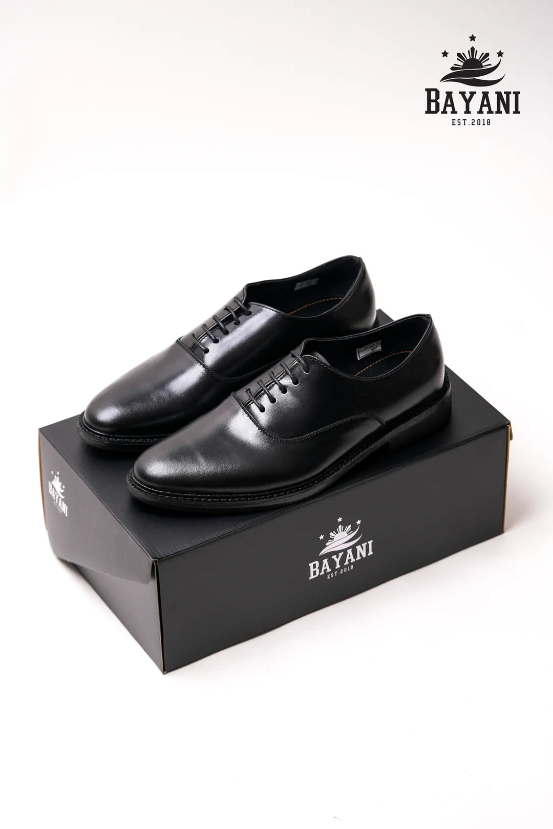 Black leather shoes on a black box with Bayani logo, on a white background
