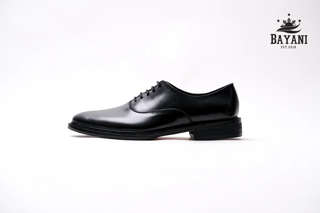 Black dress shoe on a white background with Bayani logo.
