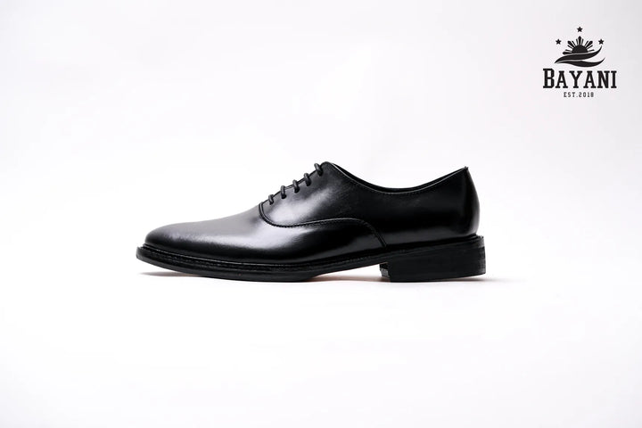 Black dress shoe on a white background with Bayani logo.
