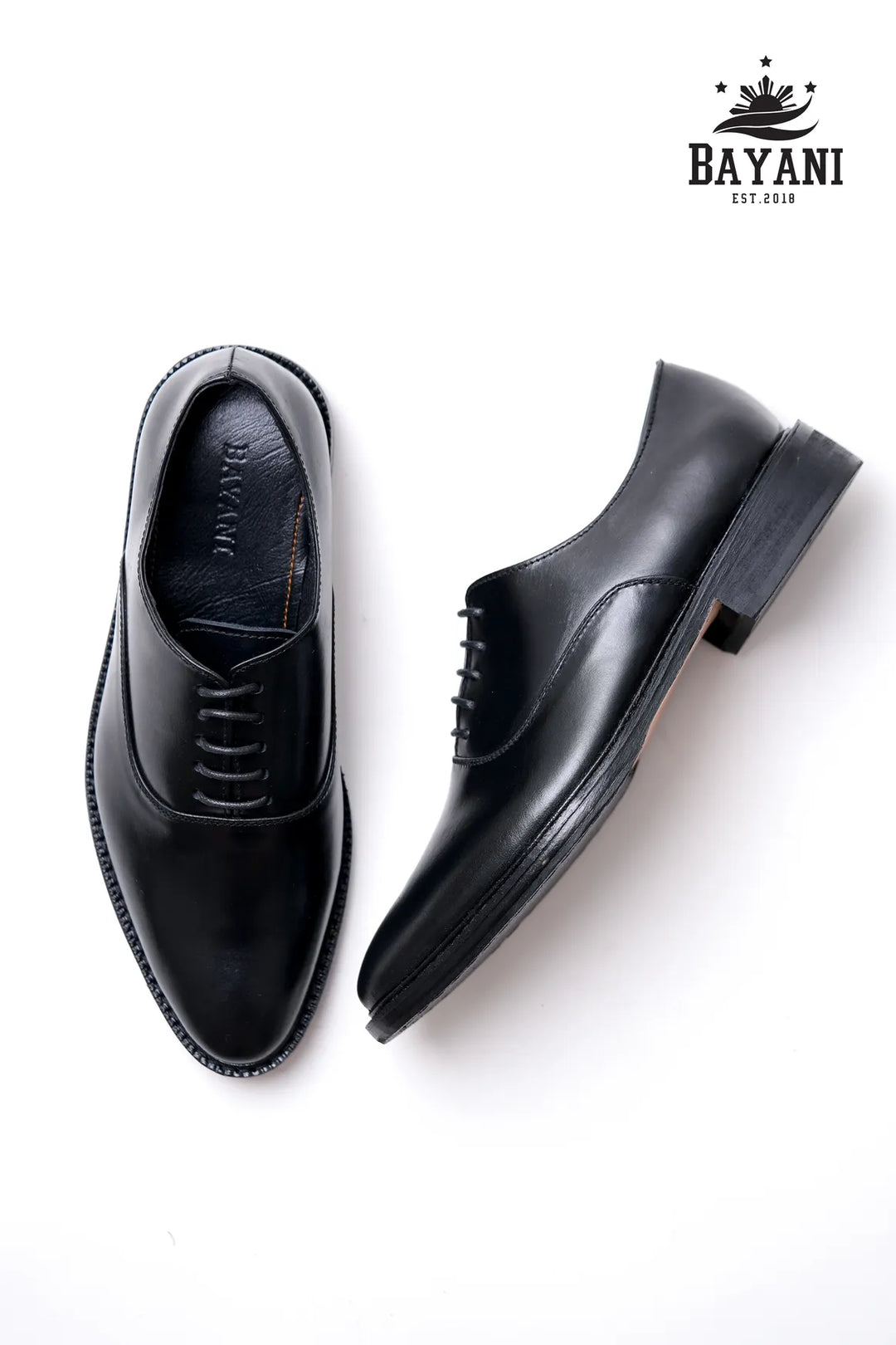Black dress shoes on a white background with Bayani logo.
