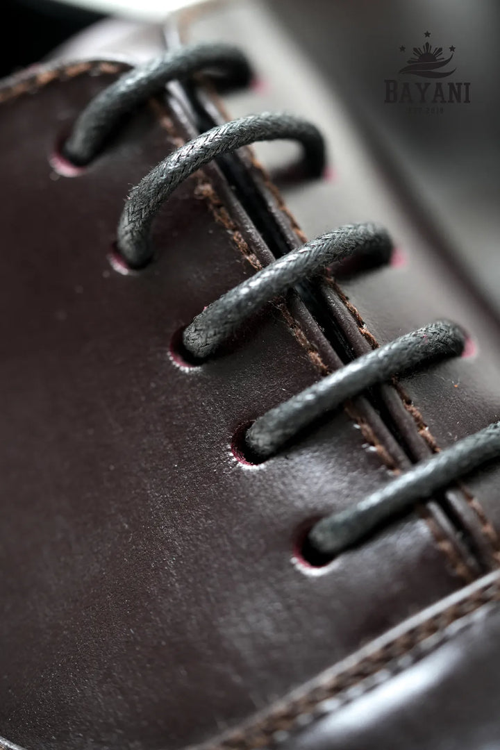 Close-up of a brown leather shoe with black laces, featuring the Bayani brand logo.
