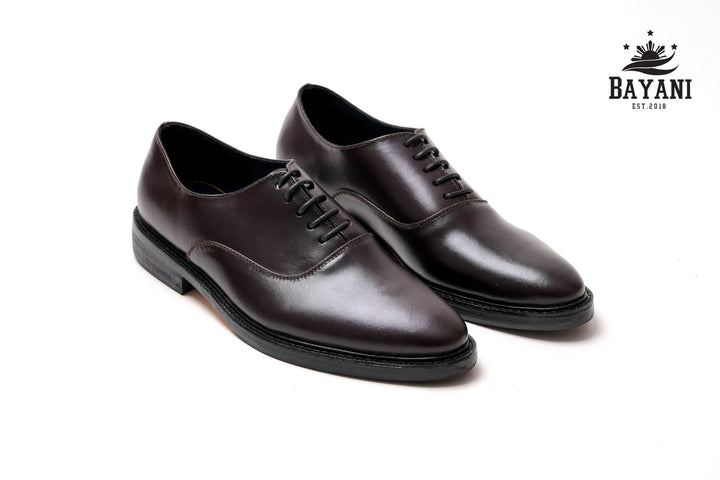 Pair of brown leather shoes on a white background with Bayani logo.
