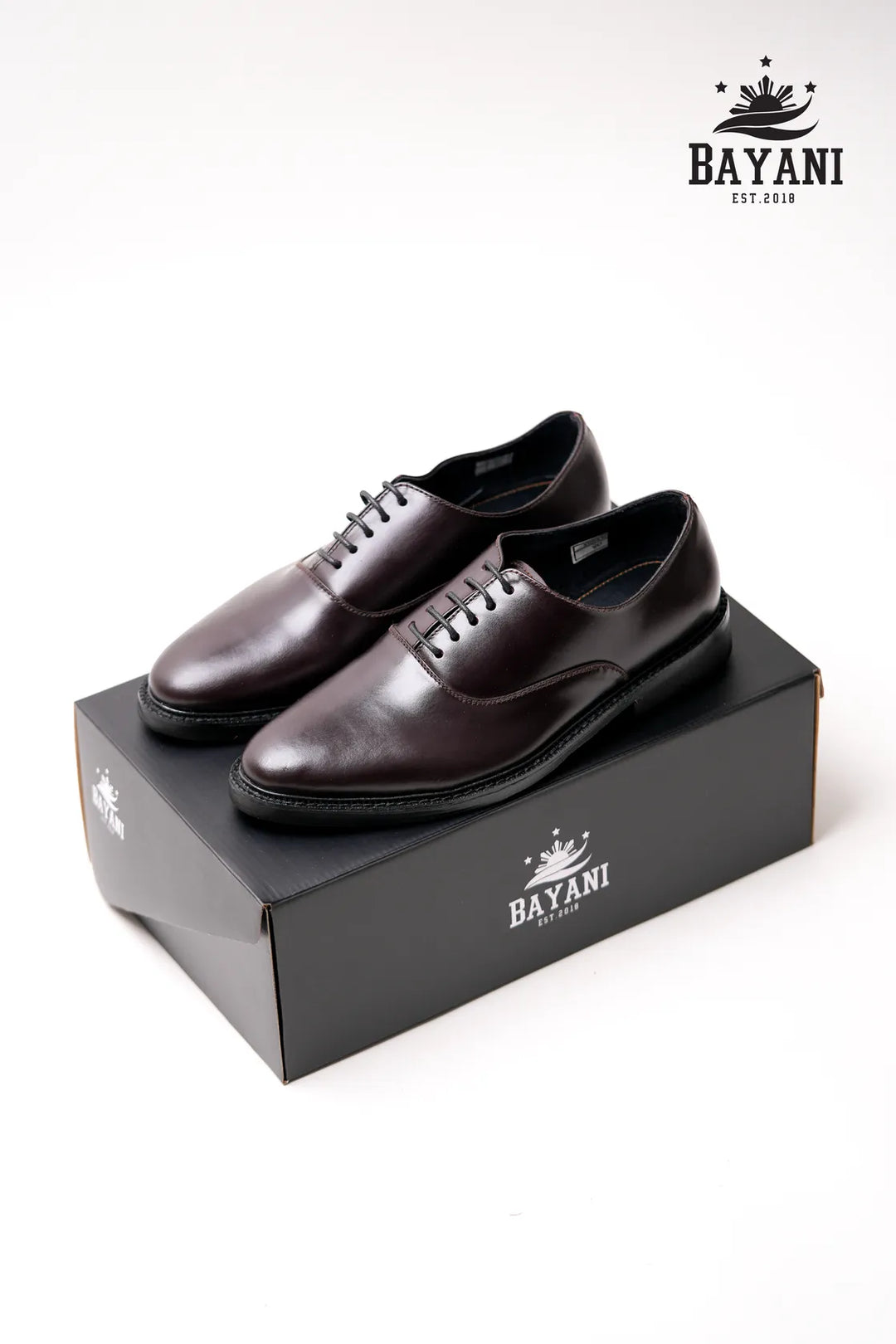 Brown dress shoes on a Bayani branded box with the Bayani logo above.
