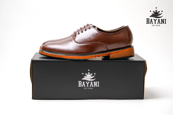 Brown leather shoe on a black box with Bayani logo, on a white background
