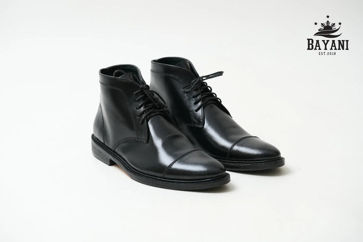 Pair of black leather dress boots on a white background with Bayani logo.

