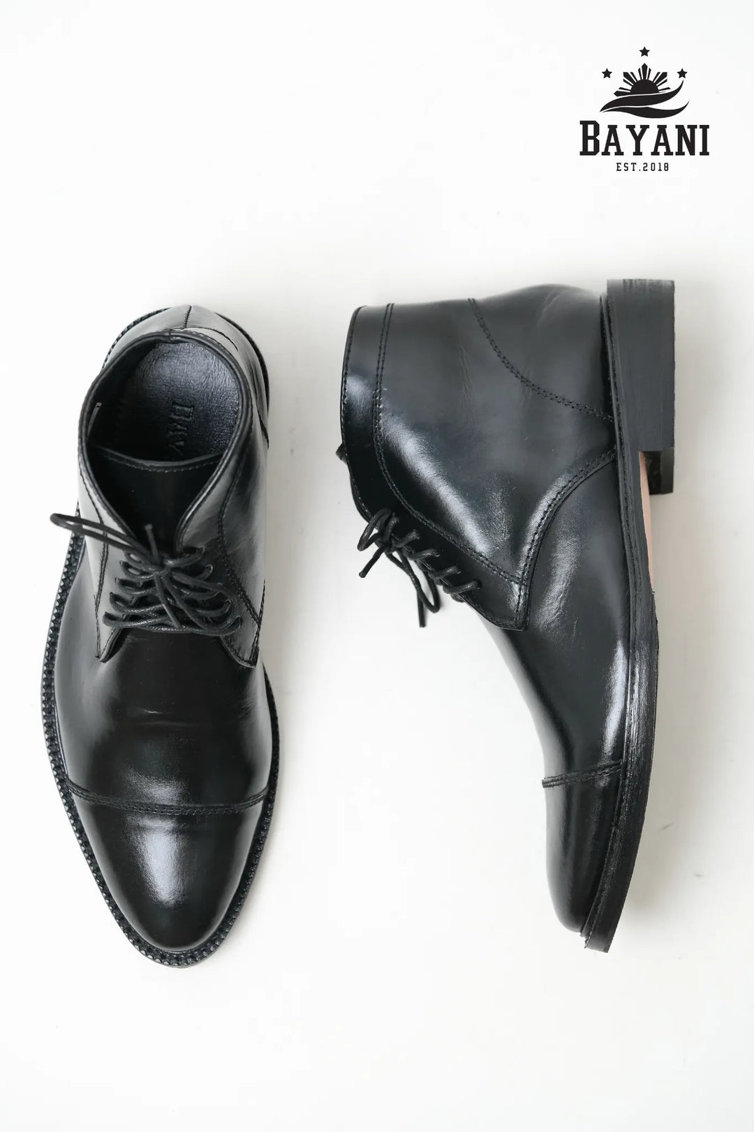 Pair of black leather shoes on a white background with Bayani logo.

