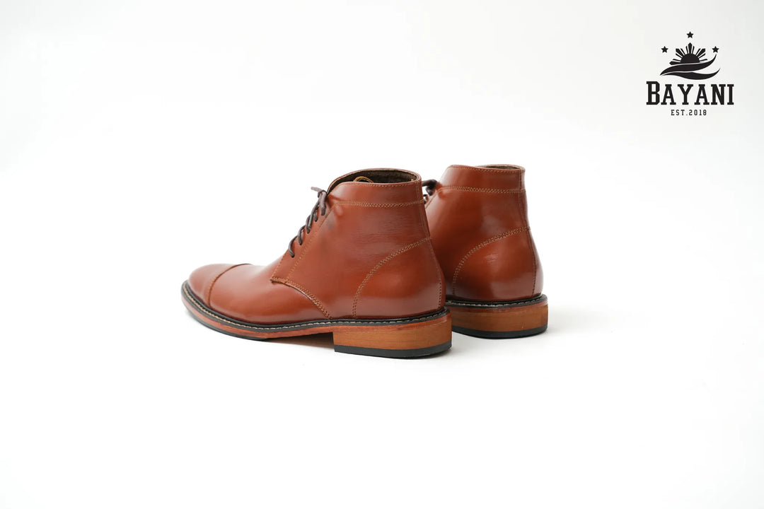 Pair of brown leather boots on a white background with Bayani logo.
