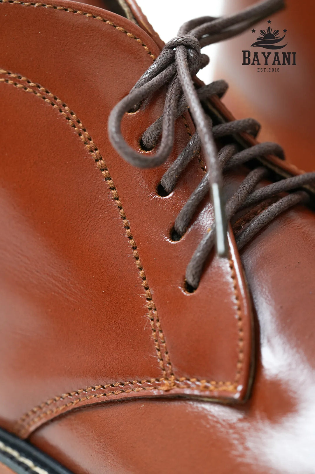 Close-up of a brown leather shoe with laces, featuring the Bayani brand logo.
