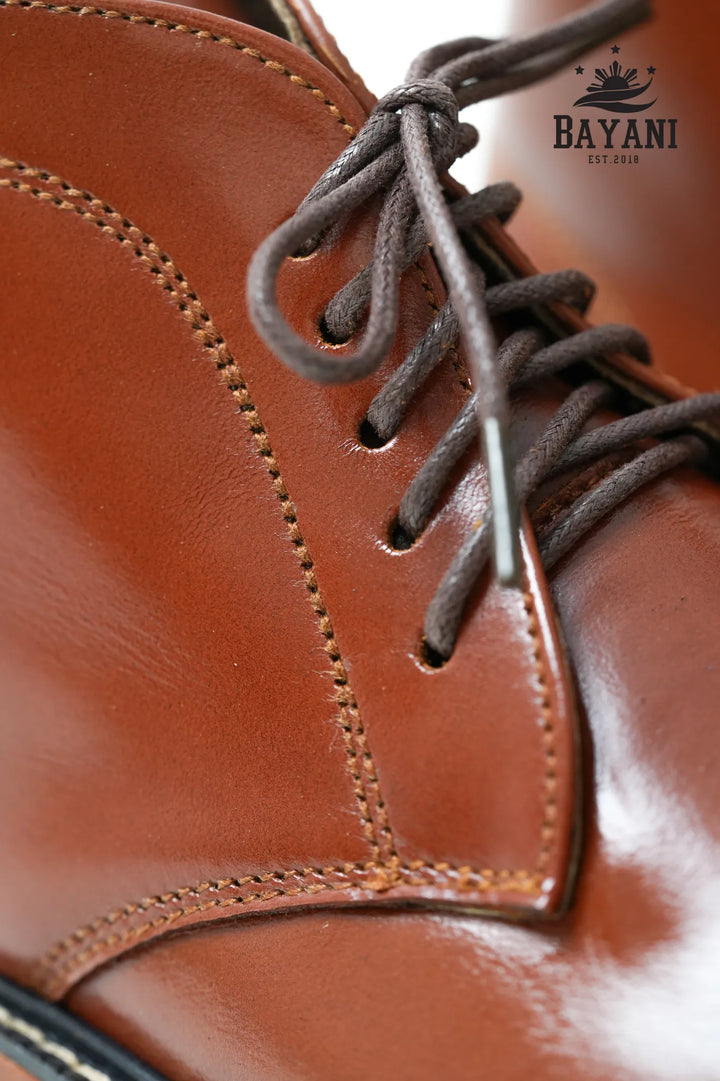 Close-up of a brown leather shoe with laces, featuring the Bayani brand logo.
