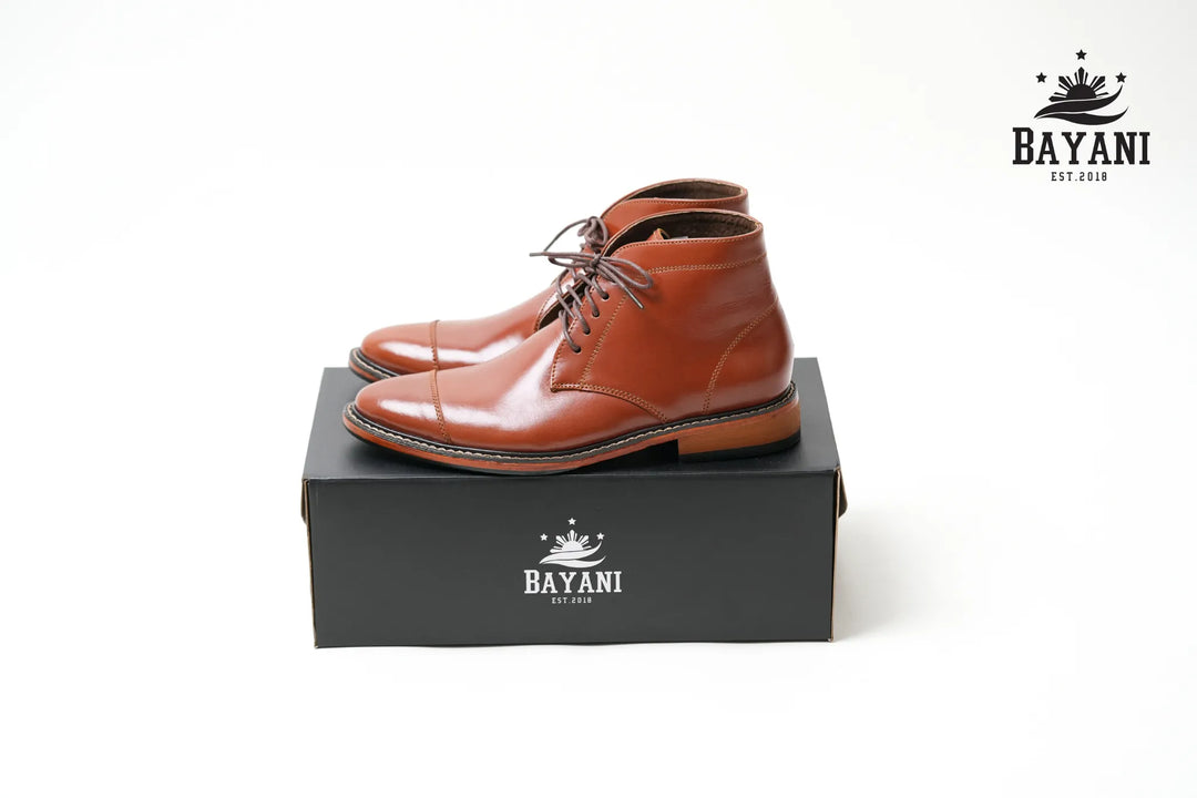 Pair of brown leather boots on a black box with Bayani logo, on a white background
