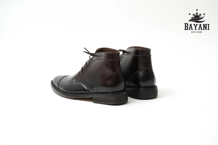 Pair of brown leather boots on a white background with Bayani logo.