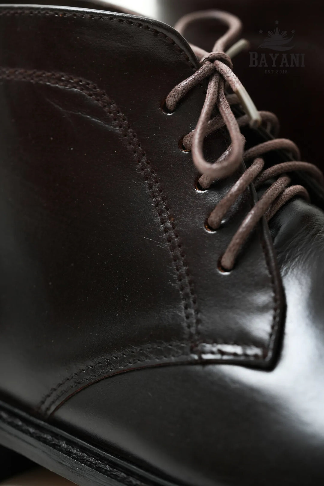Close-up of a black leather boot with brown laces on a blurred background
