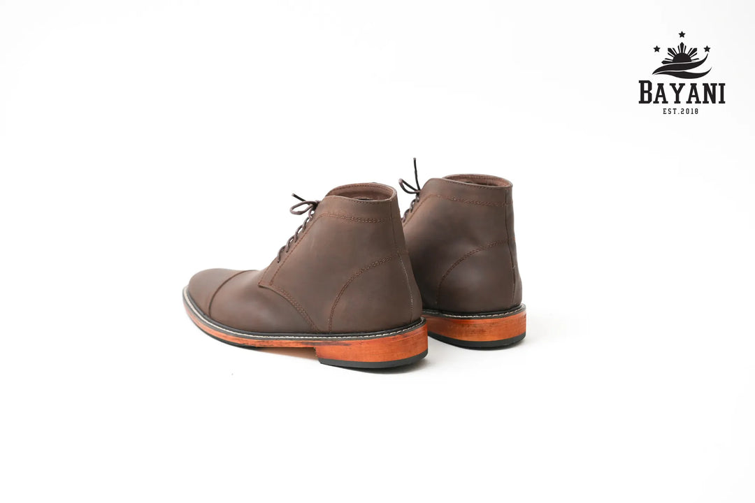 Pair of brown leather boots on a white background with Bayani logo.
