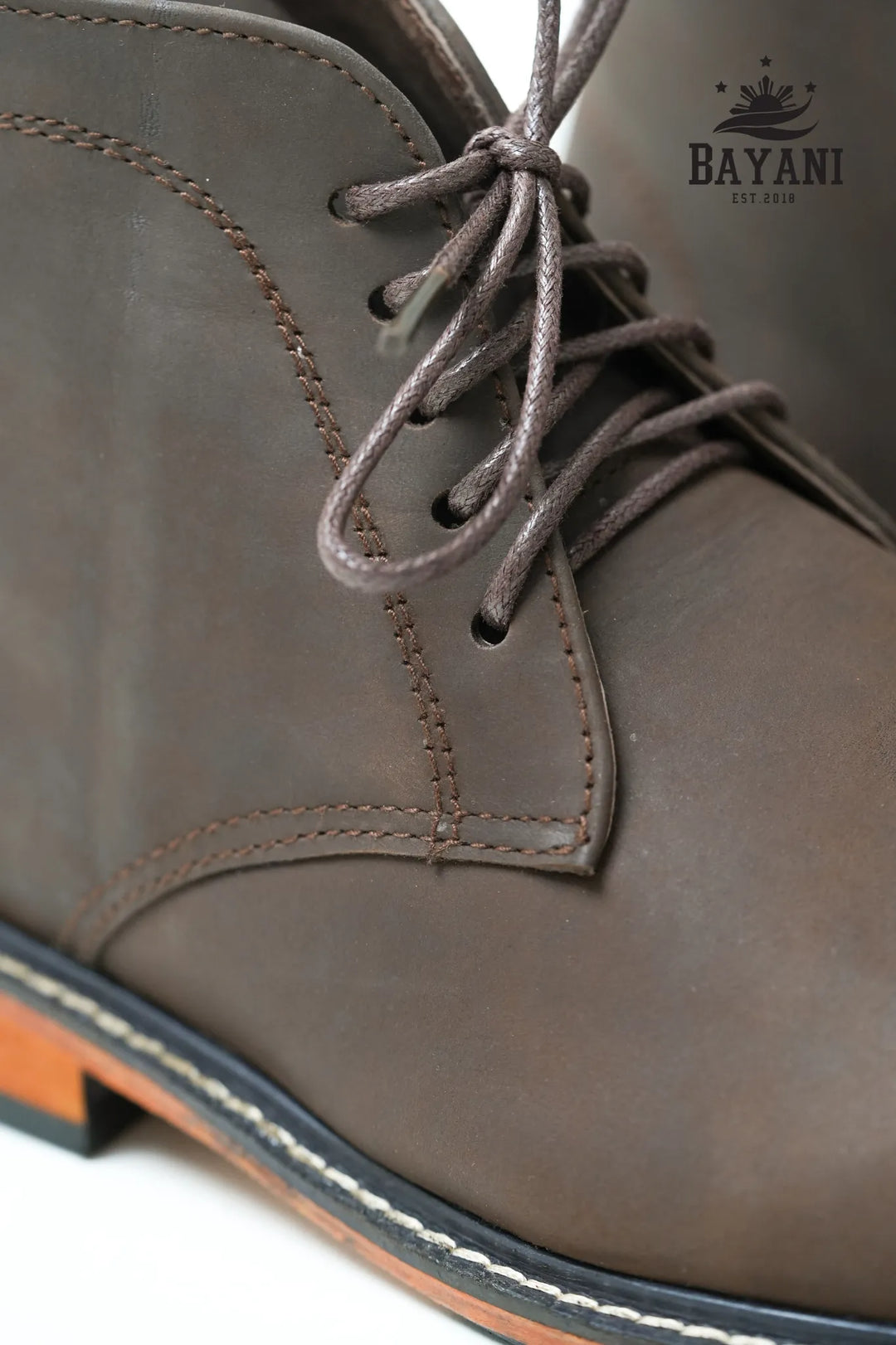 Close-up of a brown leather boot with laces, featuring the Bayani brand logo.
