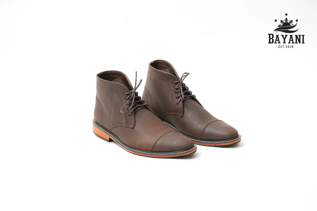 Pair of brown leather boots on a white background with Bayani logo.
