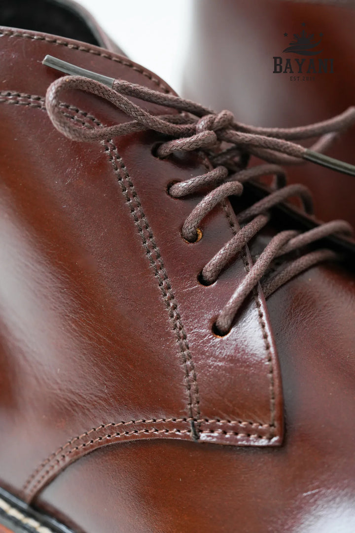 Close-up of a brown leather boot with laces, brand &