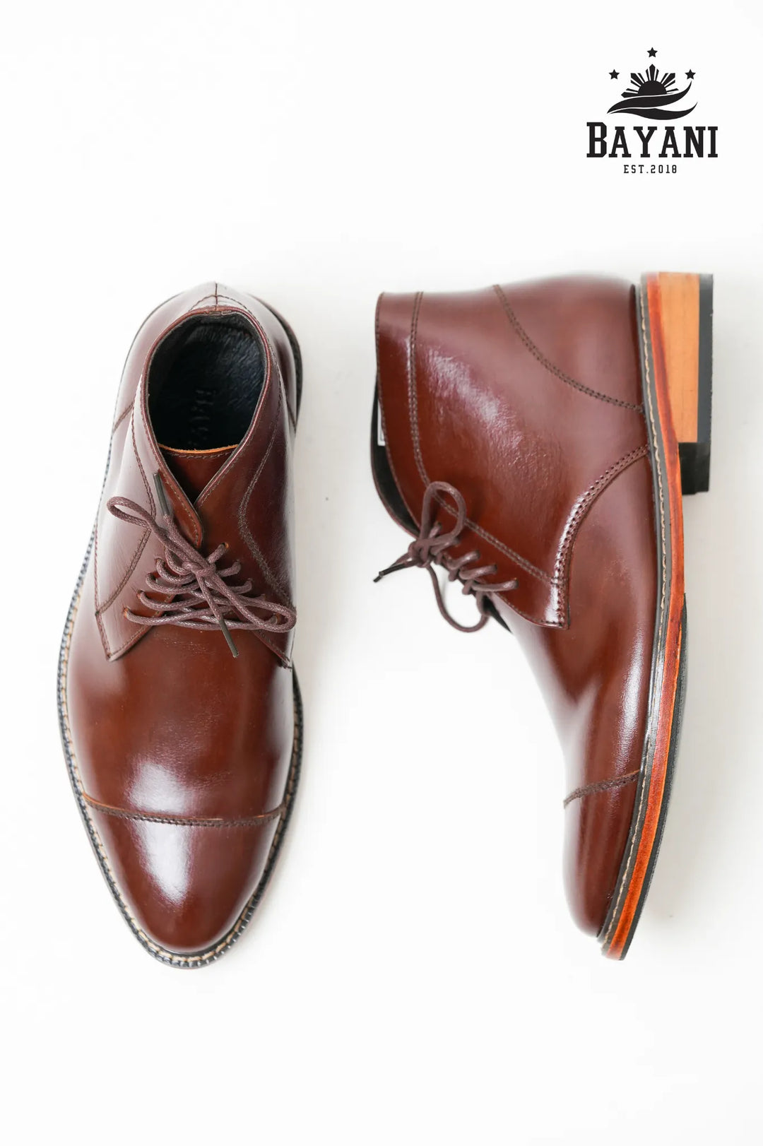 Brown leather shoes with orange accents on a white background, featuring the Bayani brand logo.
