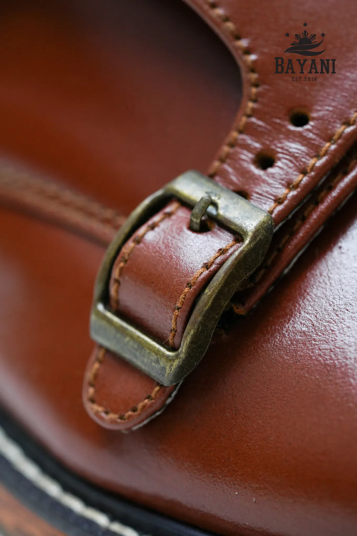 Close-up of a brown leather strap with a brass buckle, featuring the Bayani brand.
