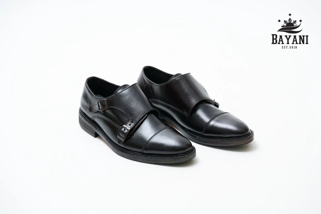 Pair of black dress shoes on a white background with Bayani logo.
