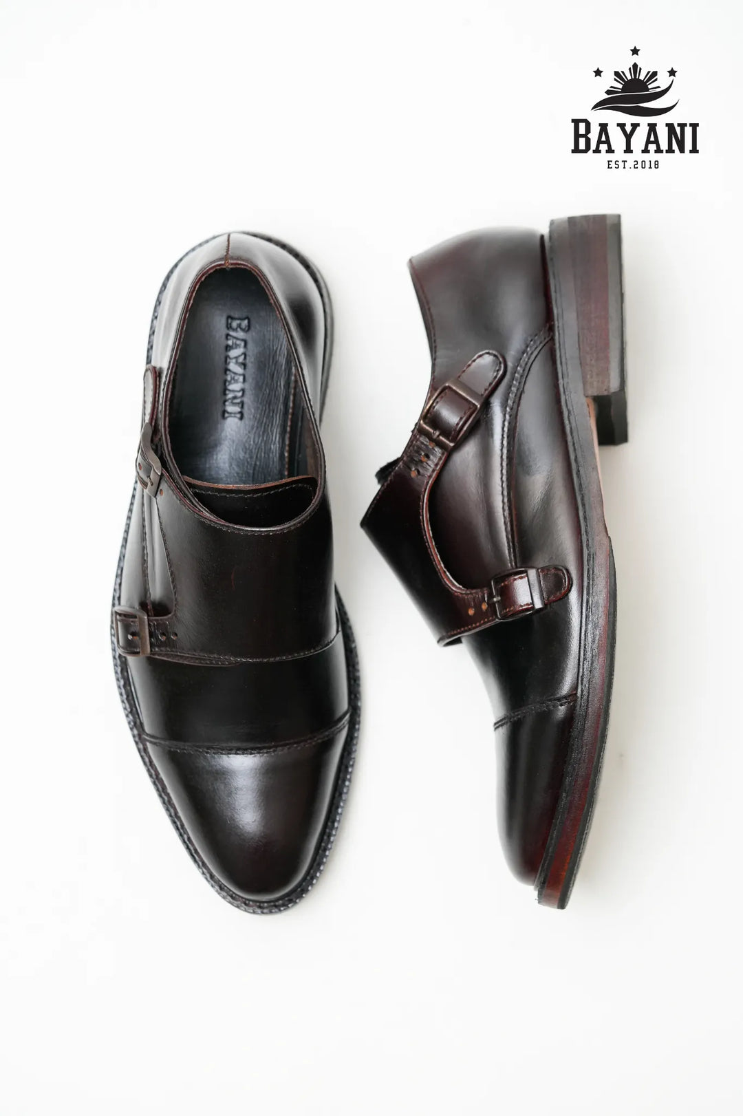 Pair of black leather shoes with brown buckles on a white background, featuring the Bayani brand logo.
